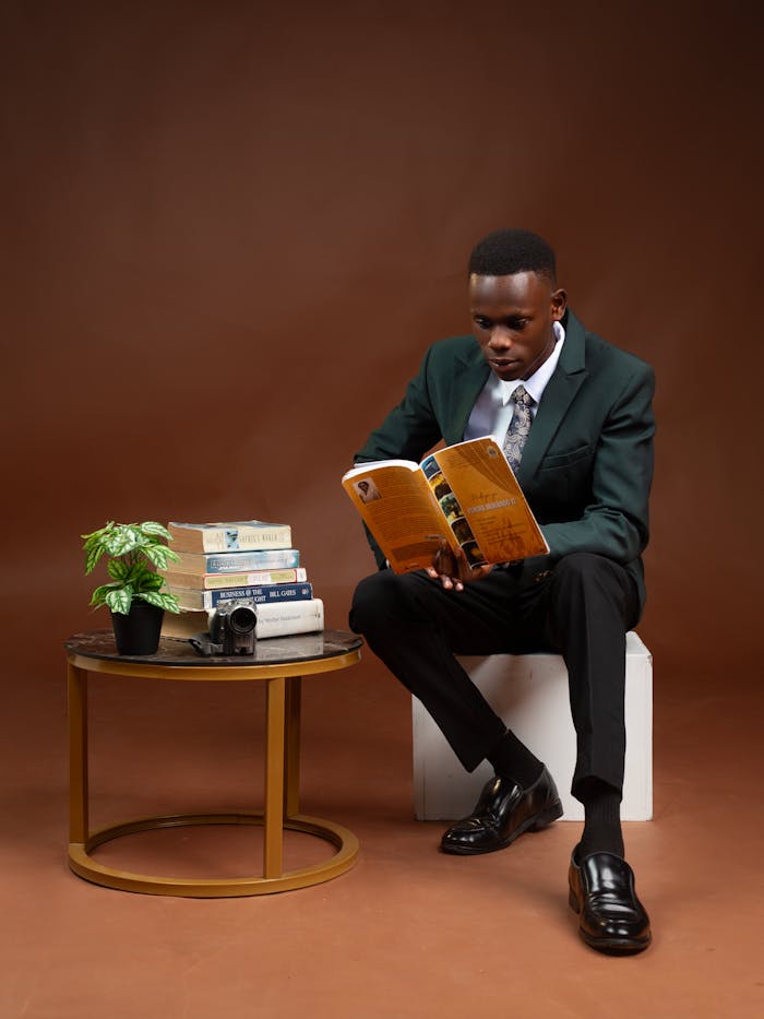 Young adult in a suit reading a book indoors with a tidy minimalist setup, promoting focus and relaxation.