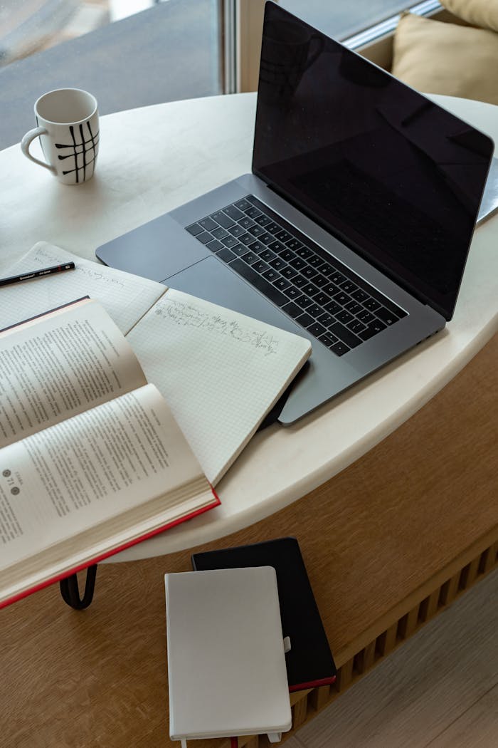 A cozy indoor workspace featuring a laptop, open book, notepad, and coffee, perfect for studying or remote work.